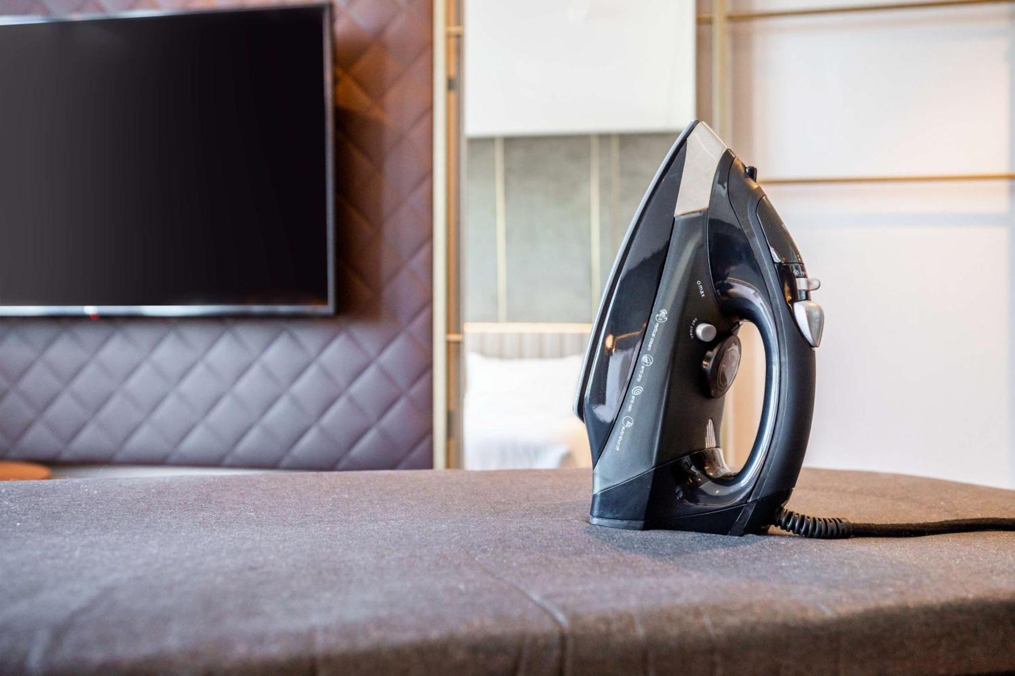 Nh Collection Copenhagen Hotel Bagian luar foto The photo shows a black iron placed on a grey ironing board, which is covered with a fabric surface. In the background, there's a large television mounted on the wall, and the setting appears to be a modern room with stylish decor, featuring a quilte