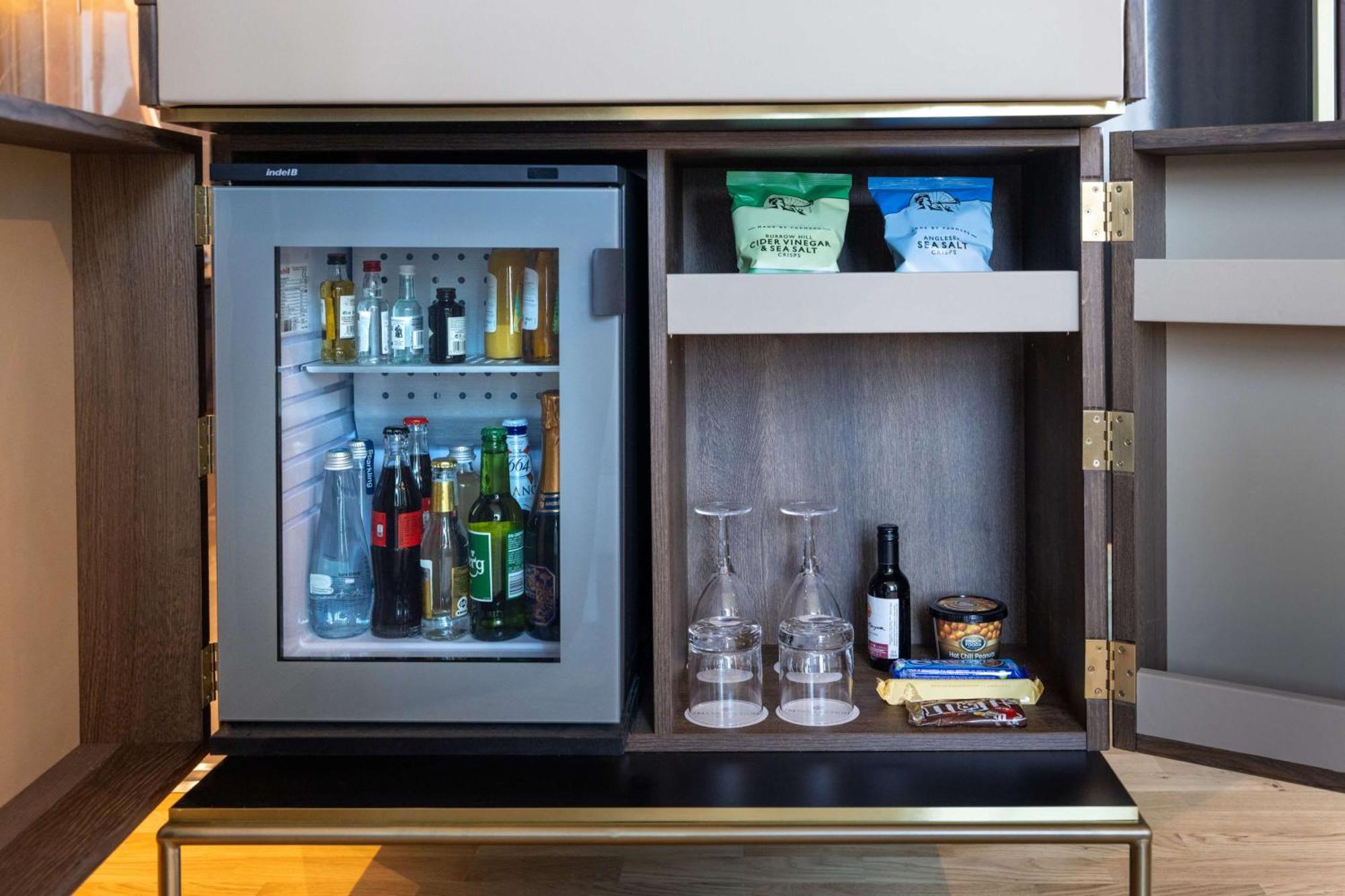 Nh Collection Copenhagen Hotel Bagian luar foto The photo shows a stylish refrigerator integrated into a cabinet. The fridge has a glass door, allowing visibility of its contents, which include various bottles and drinks. Above the fridge, there are shelves with some snacks or food items organized
